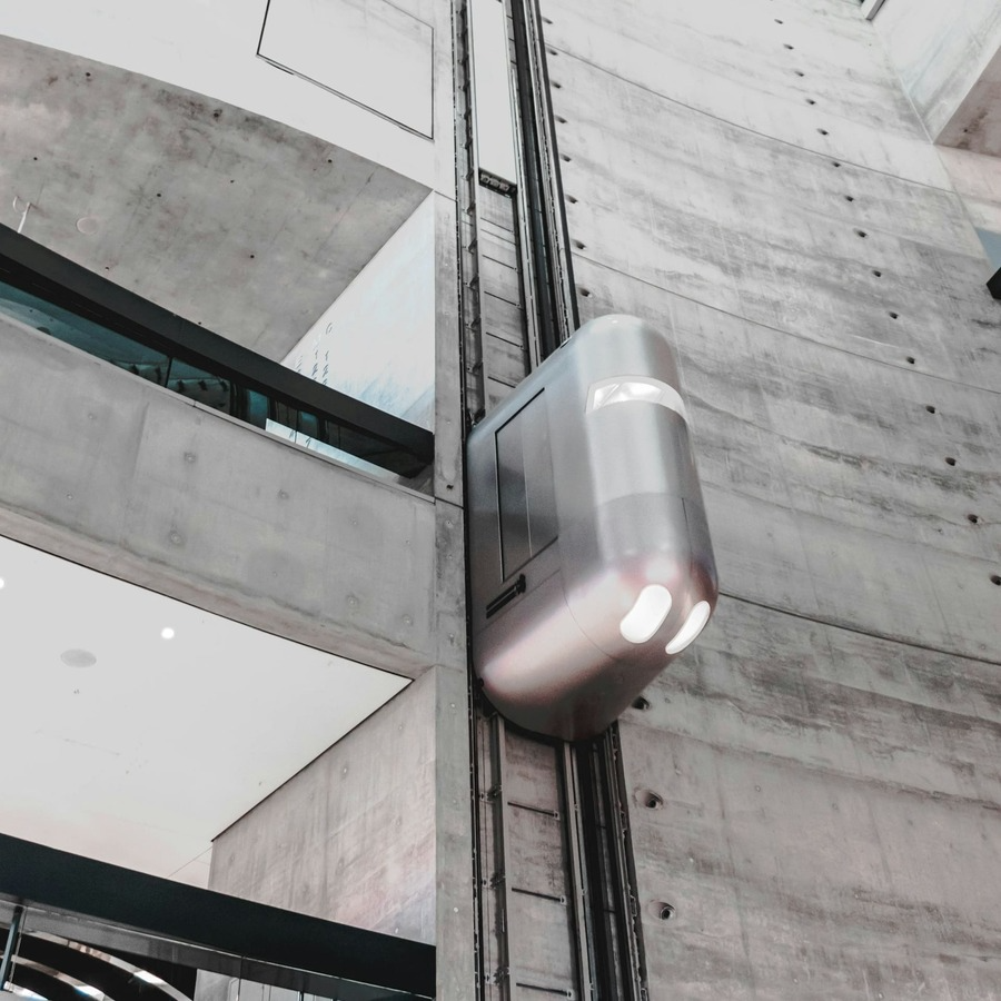 Futuristic elevator pod travelling down the side of a concrete exterior building