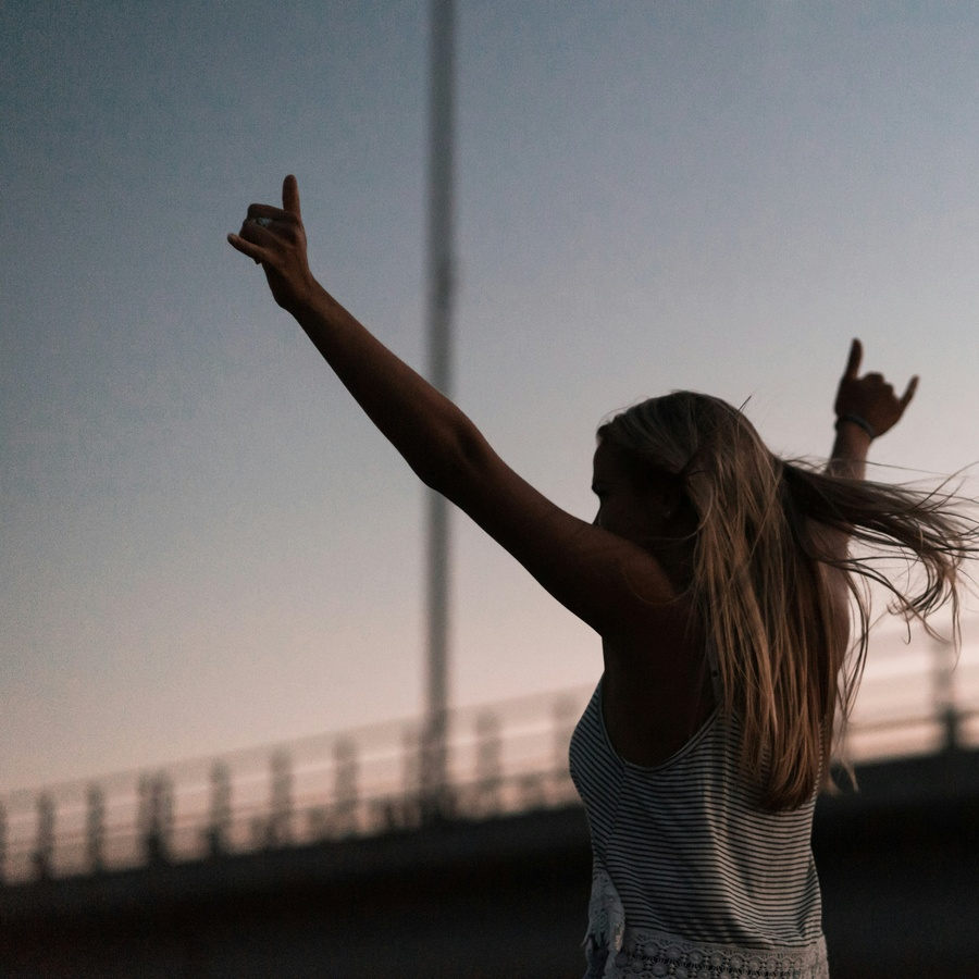 Woman running during sunrise with arms up and pointing outwards